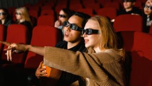 Młodzi ludzie, chłopak z dziewczyną w sali kinowej z okularami na oczach pełni emocji zachwytu podczas oglądania filmu.